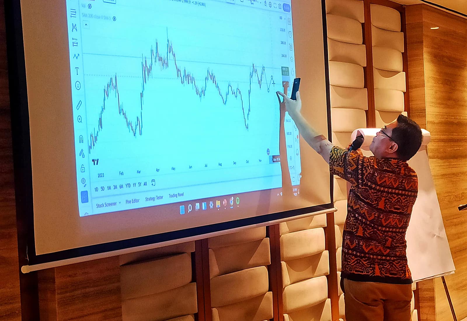 Fasilitator menunjuk grafik candlestick di layar besar saat sesi technical analysis